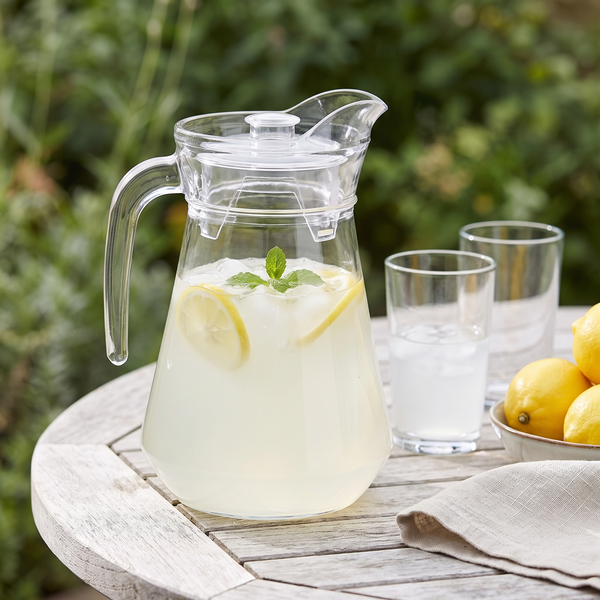 Clear plastic pitcher of lemonade with snap-on lid on a garden table in sunshine