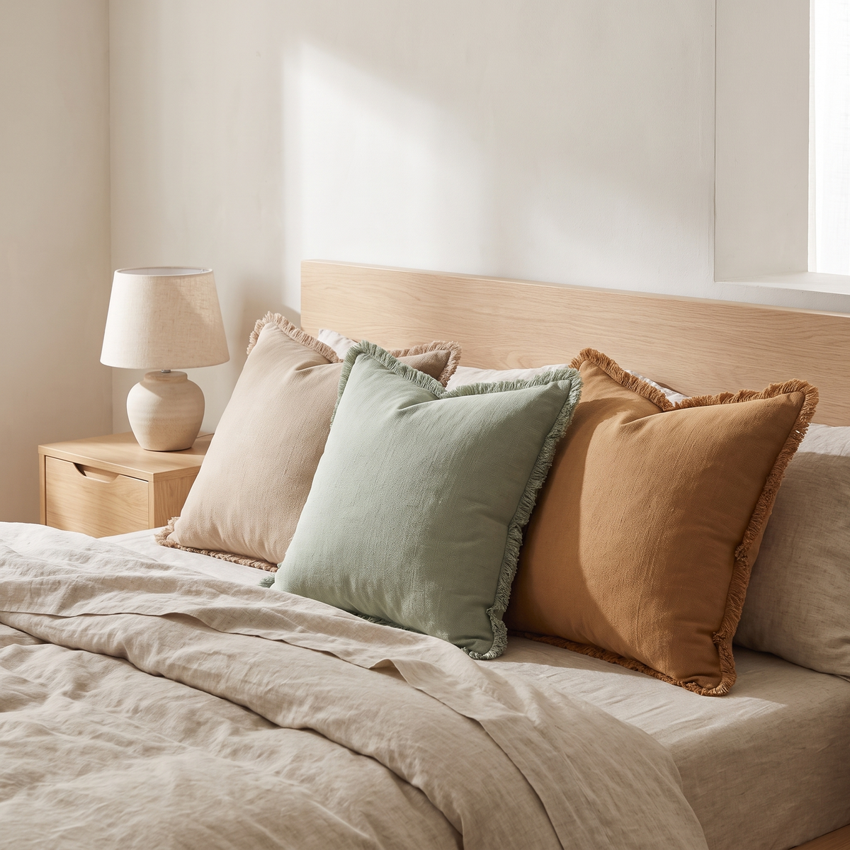 Fringed cotton cushion covers in beige, sage and caramel on a bed