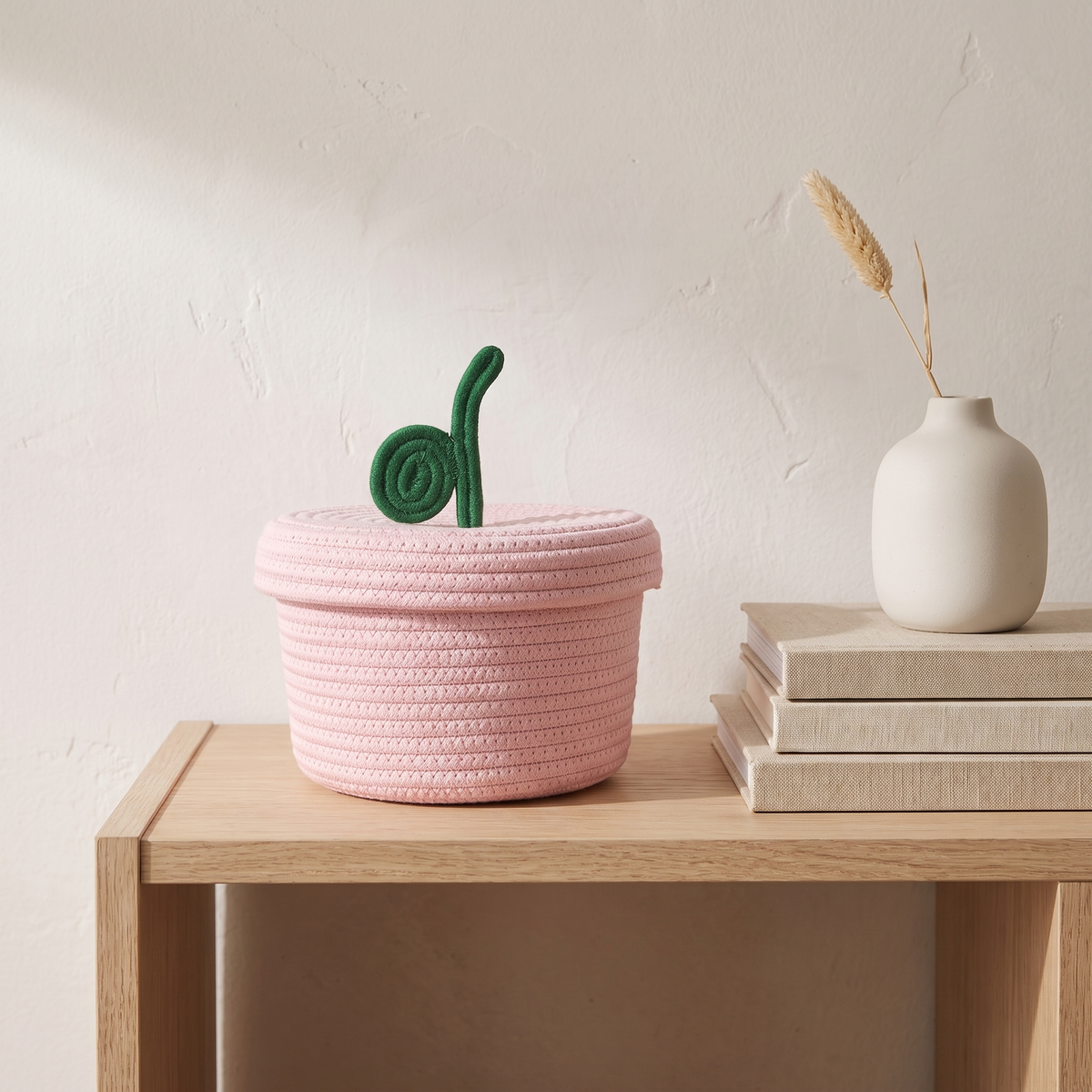 Pink cotton rope basket with leaf lid on an oak shelf