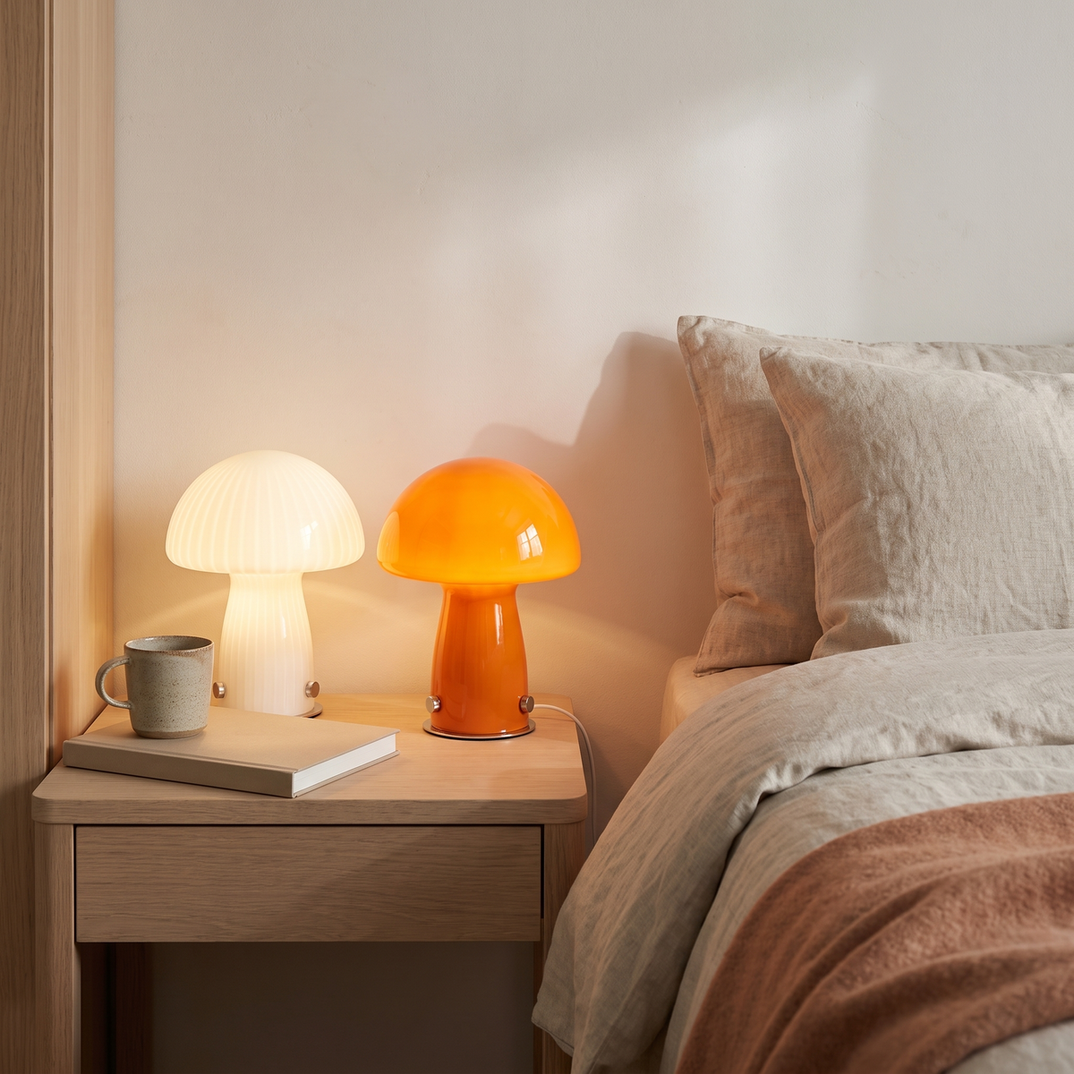 White swirl and orange glass mushroom lamps on a bedside table