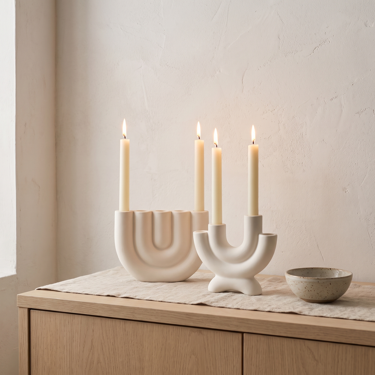 White ceramic candelabras with lit taper candles on a sideboard