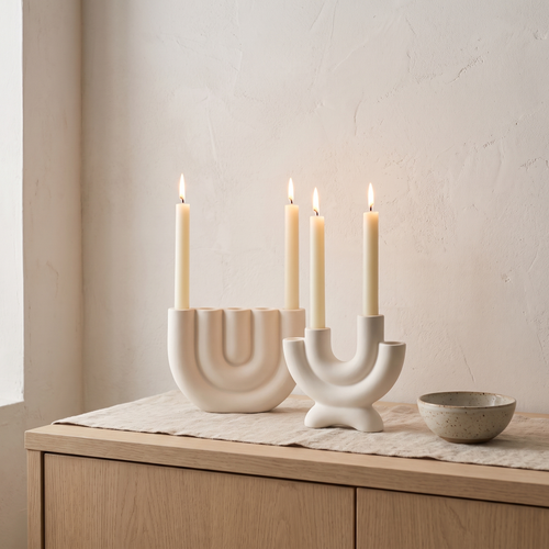 White ceramic candelabras with lit taper candles on a sideboard